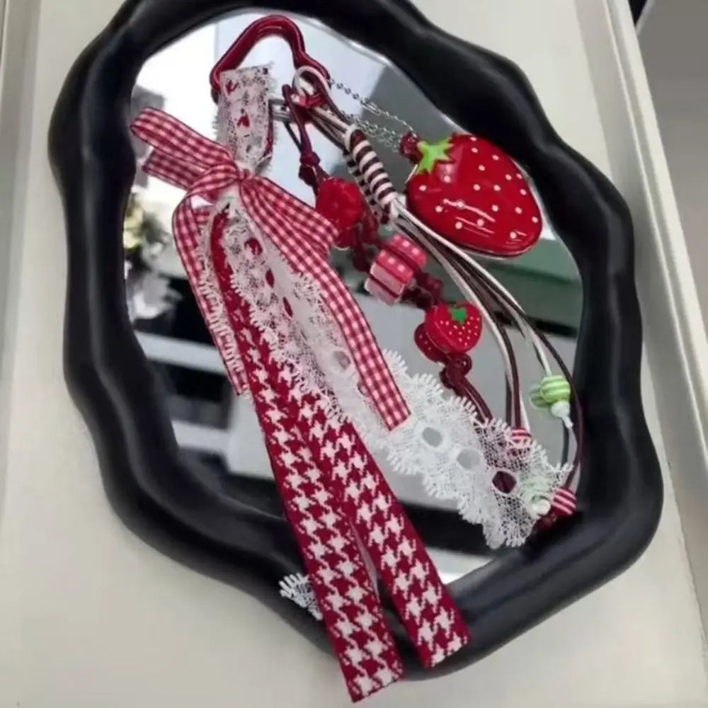 A red and white patterned strawberry bag charm keychain displayed in a black oval mirror frame.