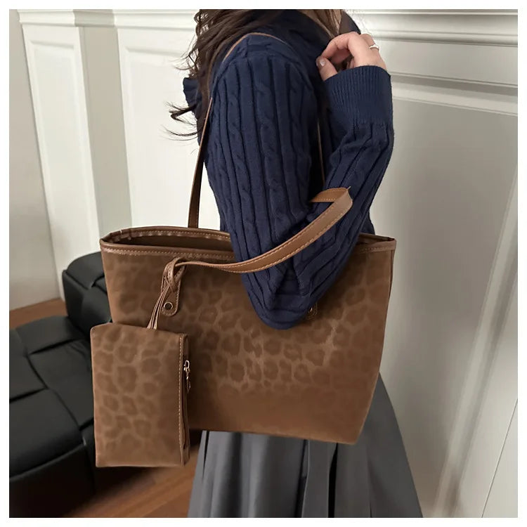 A woman holds a large brown leopard print tote bag with a tan leather strap and a dark blue knitted sweater.