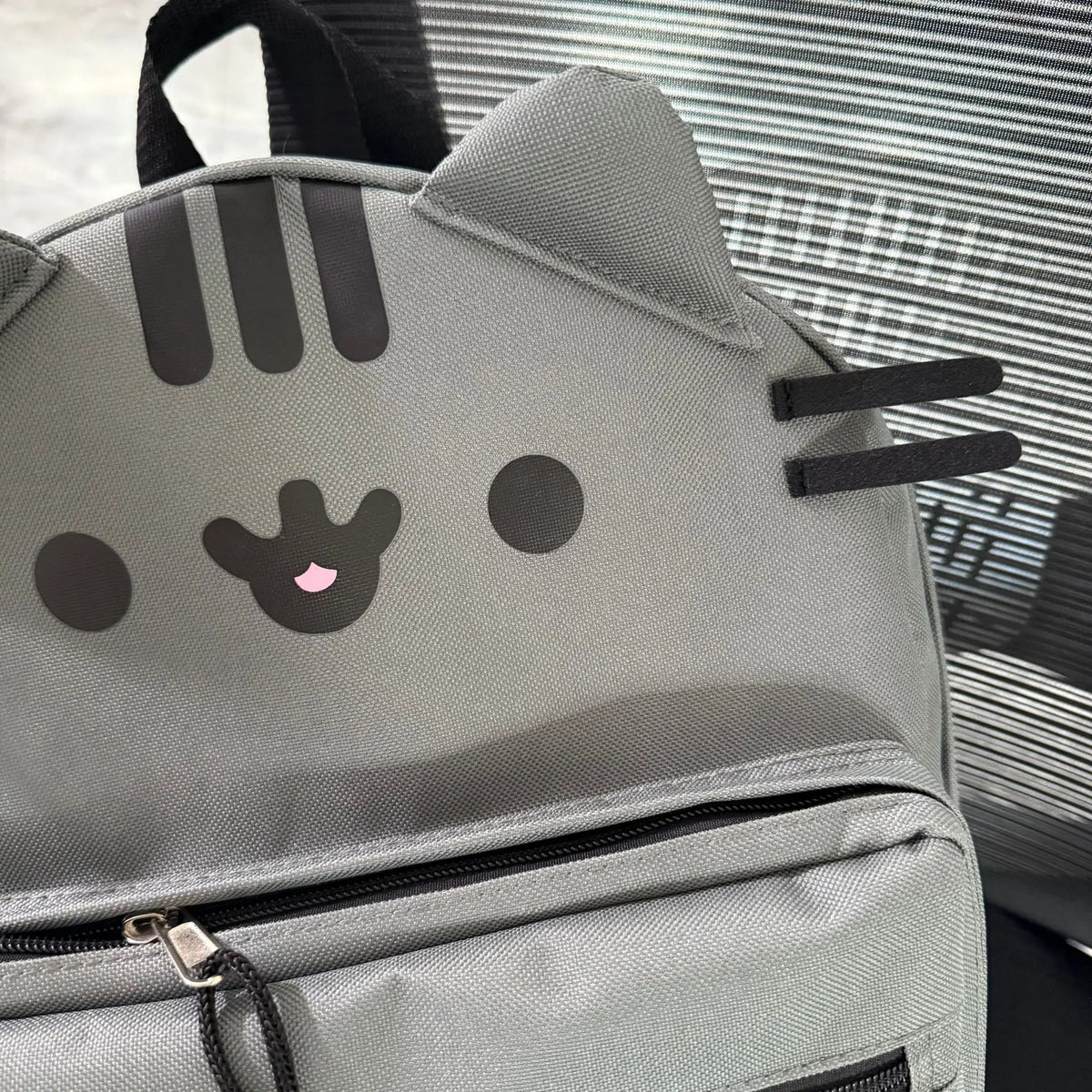 A gray Pusheen cat canvas backpack with black stripes and facial features, shown from the front.