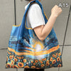 A woman holds a blue and orange floral print nylon shopping tote with a shoulder strap against a gray background.