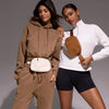 A woman models an ivory fleece crossbody belt bag with a white top and brown sweatpants.