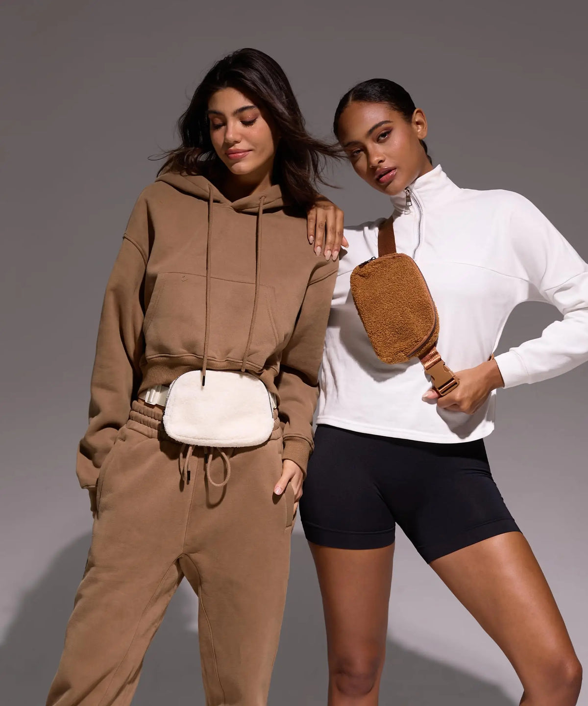 A woman models an ivory fleece crossbody belt bag with a white top and brown sweatpants.