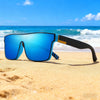 A pair of bright blue square sport sunglasses resting on golden sand near the ocean.