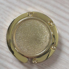 A round, gold-colored metal object with a textured surface and small fasteners.