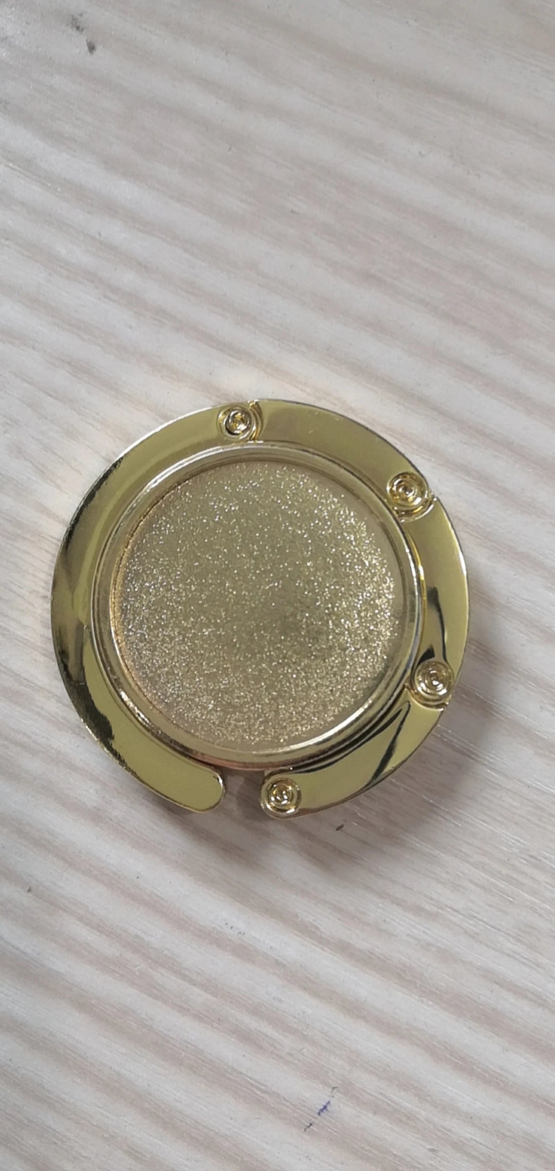 A round, gold-colored metal object with a textured surface and small fasteners.