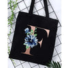 Black canvas tote bag featuring a large gold initial F with blue floral accents