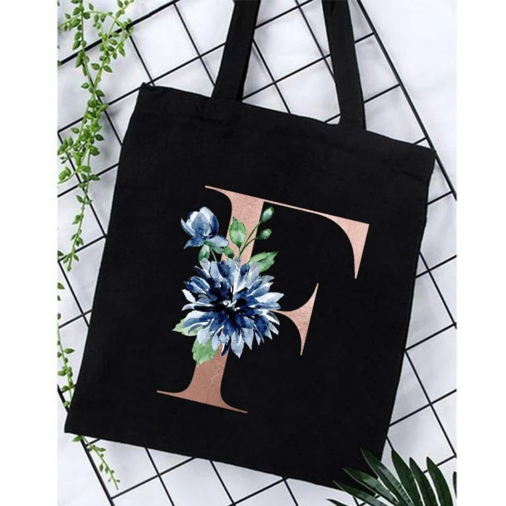 Black canvas tote bag featuring a large gold initial F with blue floral accents