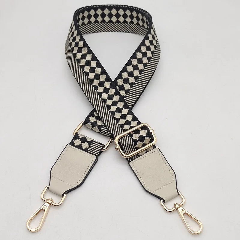 A black and white checkered braided nylon bag strap with beige leather accents and metal hooks.