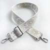 A beige and gold patterned fabric strap for a crossbody bag, shown in an 'X' shape.