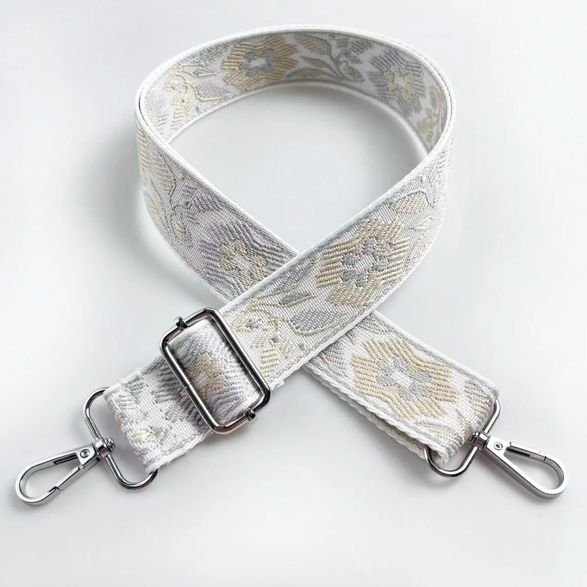 A beige and gold patterned fabric strap for a crossbody bag, shown in an 'X' shape.