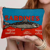 Un sac de maquillage bleu sarcelle avec un motif sardine noir et blanc est tenu par une personne.