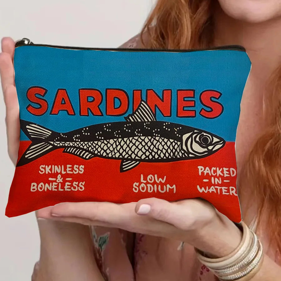 Un sac de maquillage bleu sarcelle avec un motif sardine noir et blanc est tenu par une personne.