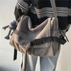 Una mujer lleva un bolso cruz de lona beige con tiras negras y un pequeño juguete de peluche gris.