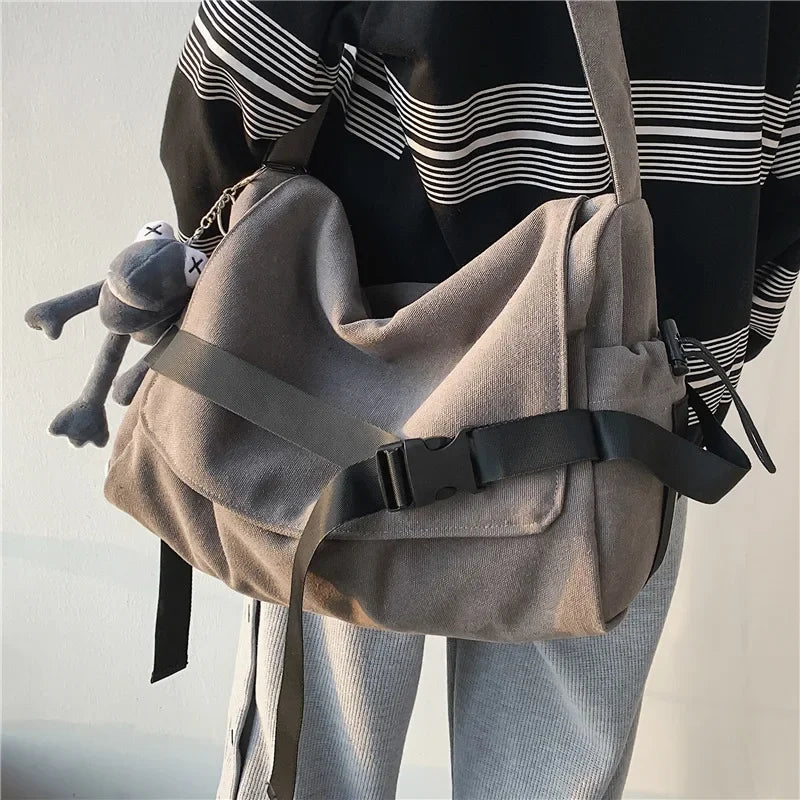 Una mujer lleva un bolso cruz de lona beige con tiras negras y un pequeño juguete de peluche gris.