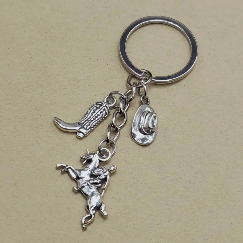 Silver keychain set featuring a cowboy boot, hat, and horseshoe charms.
