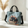 Helles blaues Taschentasche mit Blumen-Katzenmuster, orange-schwarzer Katzenillustration und schwarzen Riemen.