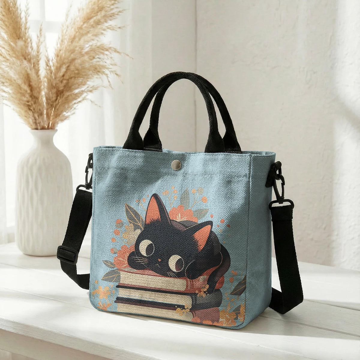 Helles blaues Taschentasche mit Blumen-Katzenmuster, orange-schwarzer Katzenillustration und schwarzen Riemen.