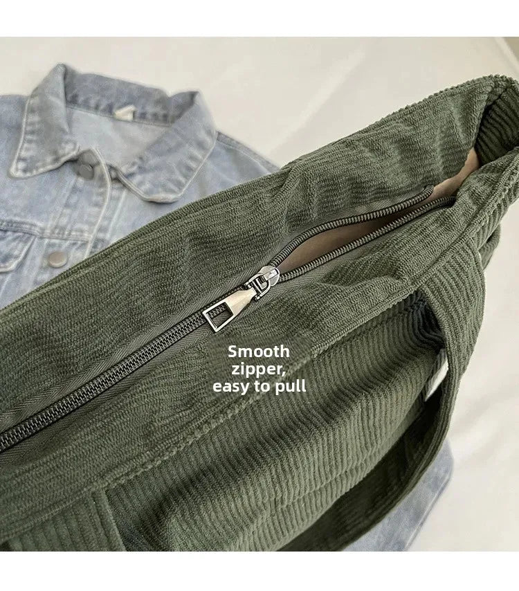 A close-up of a dark olive green corduroy shoulder bag with a zipper, shown against a light background.