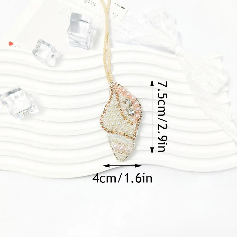 A hand sewn rhinestone beaded bag charm hanging from a gold thread against a white background.