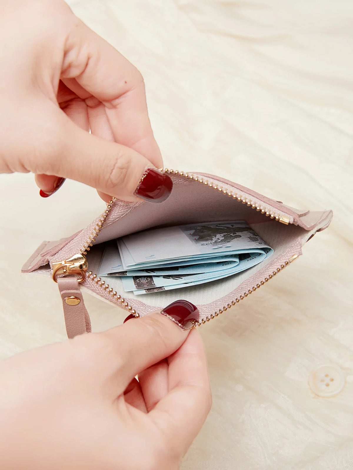 Une main ouvre un portefeuille en cuir PU rose minimaliste pour montrer son contenu.