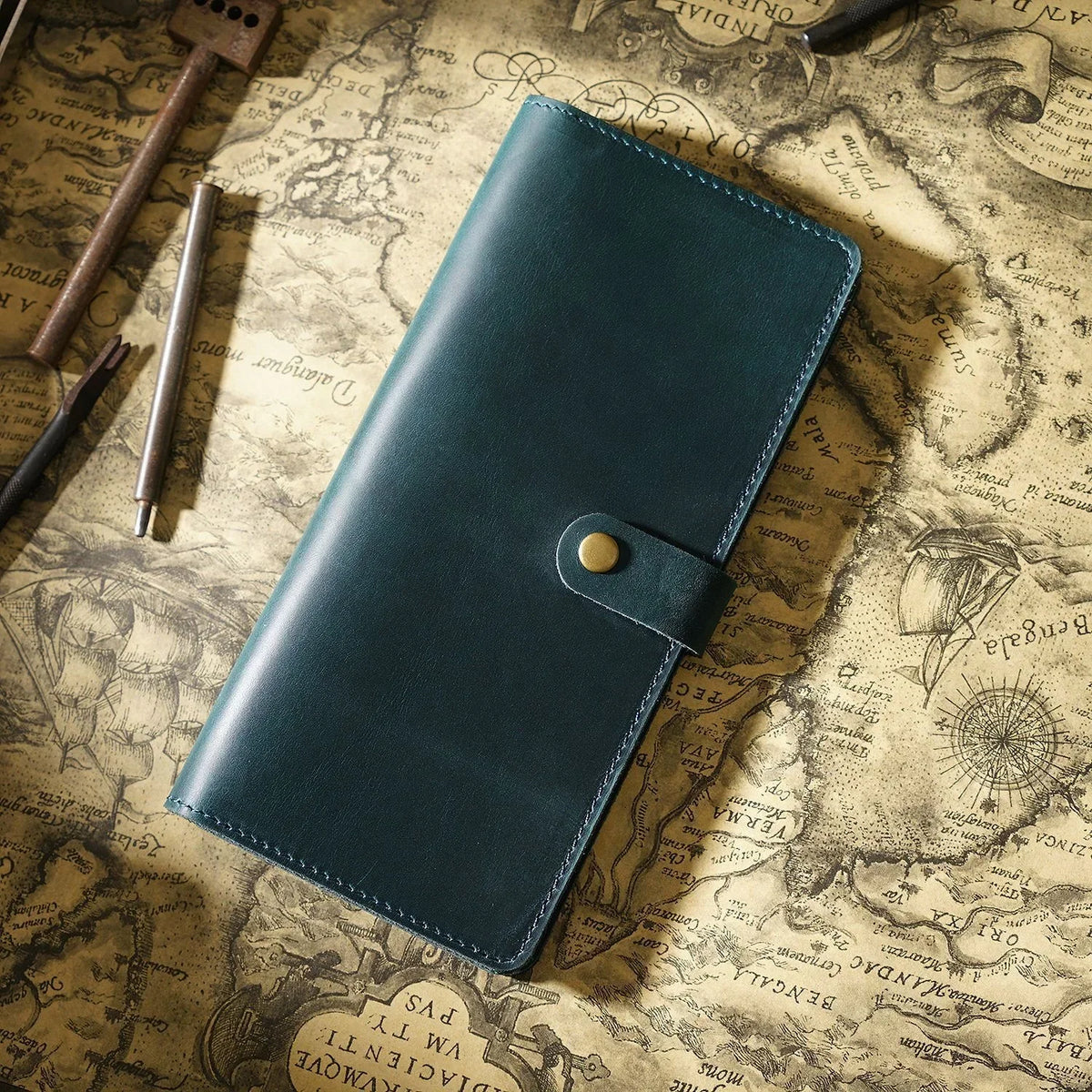 A dark teal genuine leather long bi-fold wallet with a snap closure resting on an old map background.