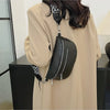 A woman holds a black PU leather multi-pocket crossbody bag with a patterned strap against a light beige coat.