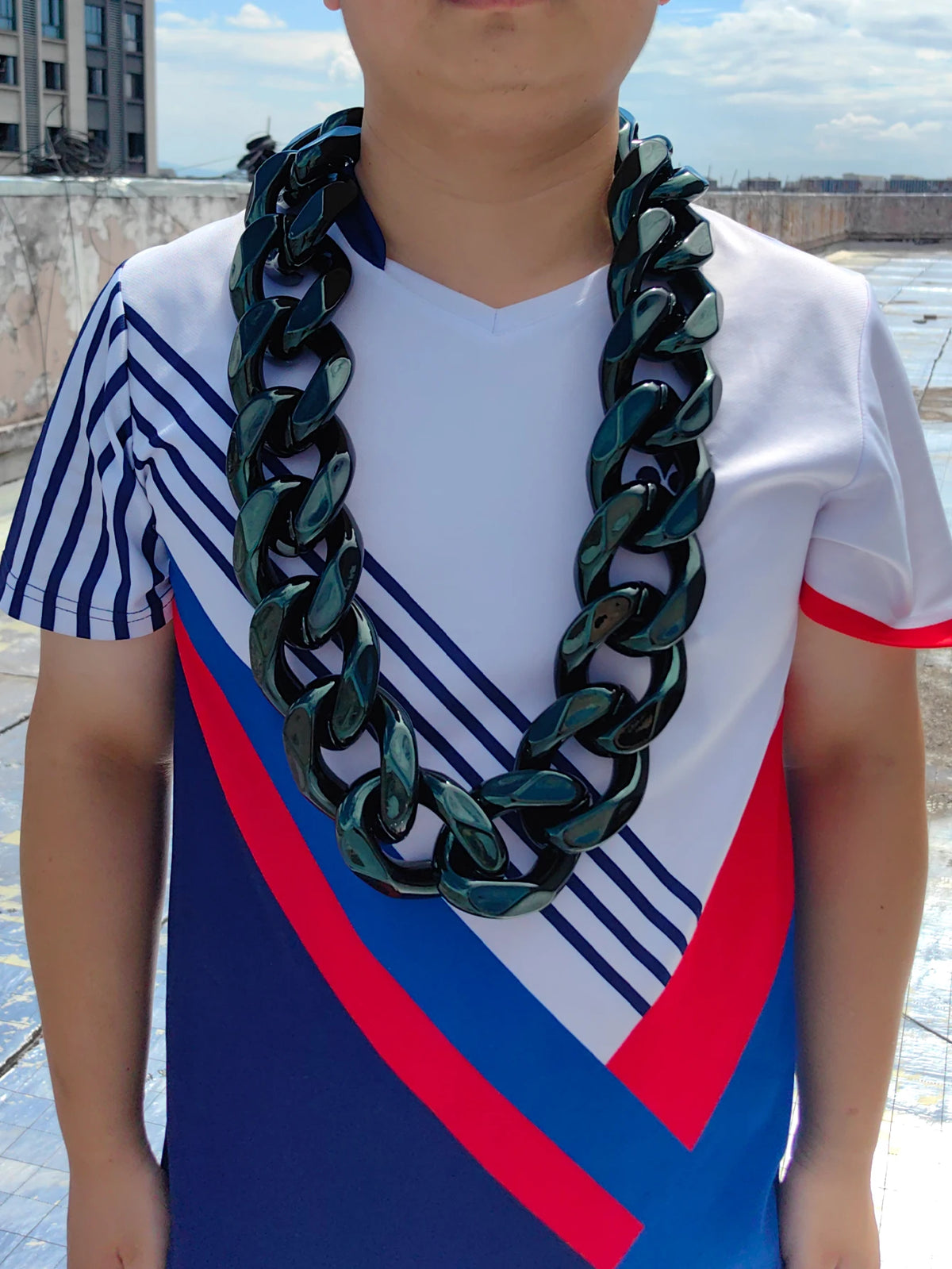 A young male wearing a chunky gold acrylic Cuban link necklace for men against an outdoor background.