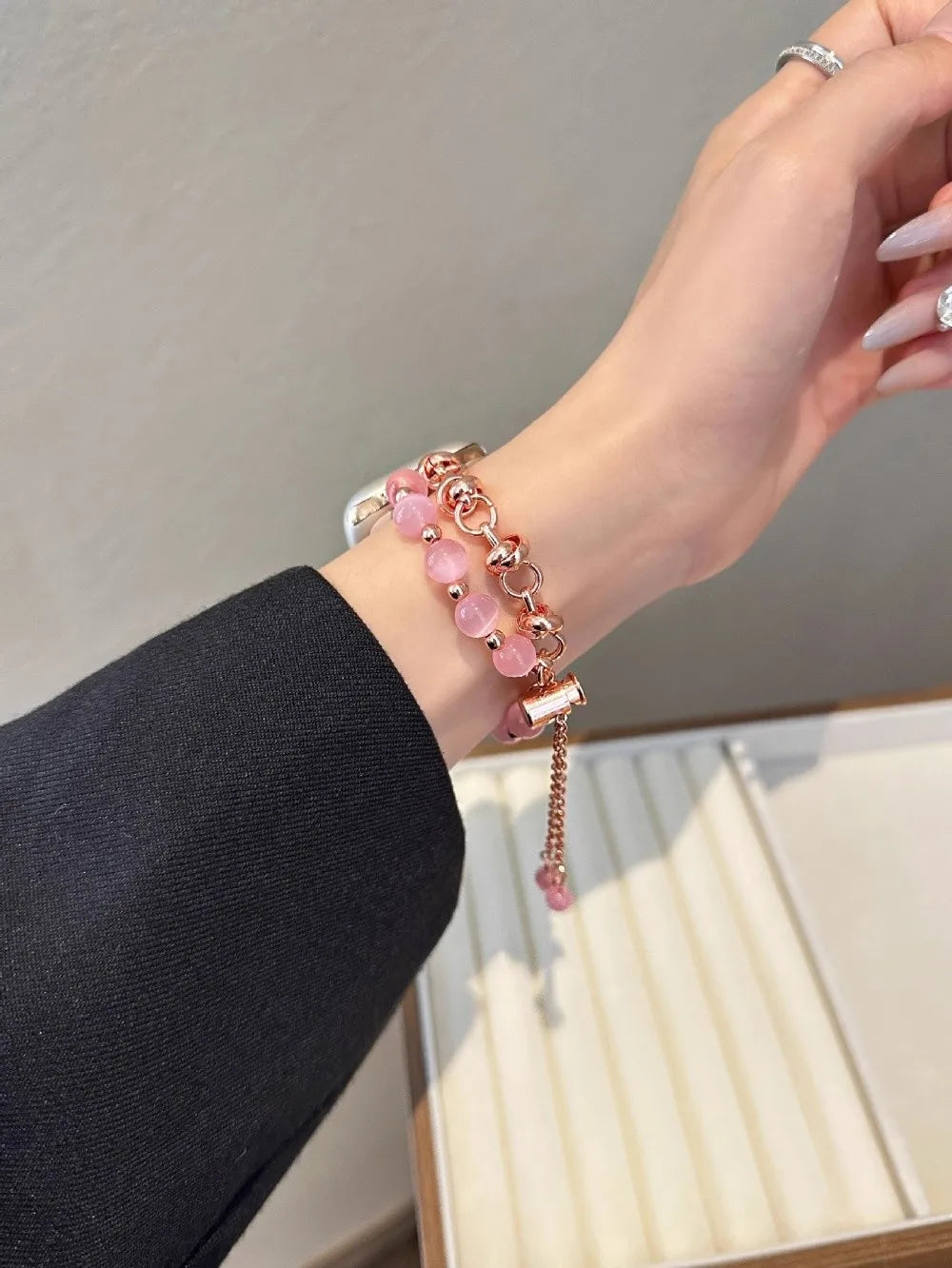 Nahaufnahme des Handgelenks einer Frau mit einem verstellbaren Metallarmband aus rosa Kristallperlen.