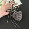 A black leather and silver leopard print plush heart pendant keychain is held in a person's hand.
