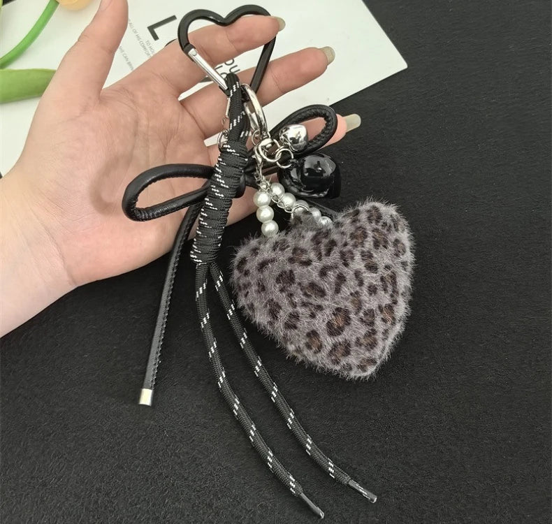 A black leather and silver leopard print plush heart pendant keychain is held in a person's hand.