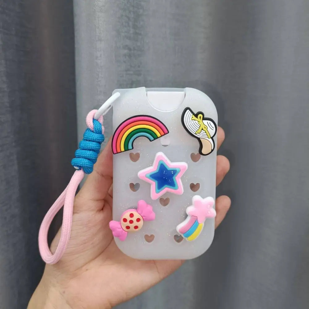 A clear silicone protective case for a hand sanitizer spray featuring a rainbow, star, and feather charm attached to a pink c