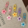 A collection of colorful resin flower keychains with metal clasps in pink, yellow, purple, and blue.