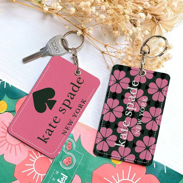 Porta tarjetas llavero de patrón rosa y negro con diseño de trébol y el nombre Kate Spade sobre fondo blanco.