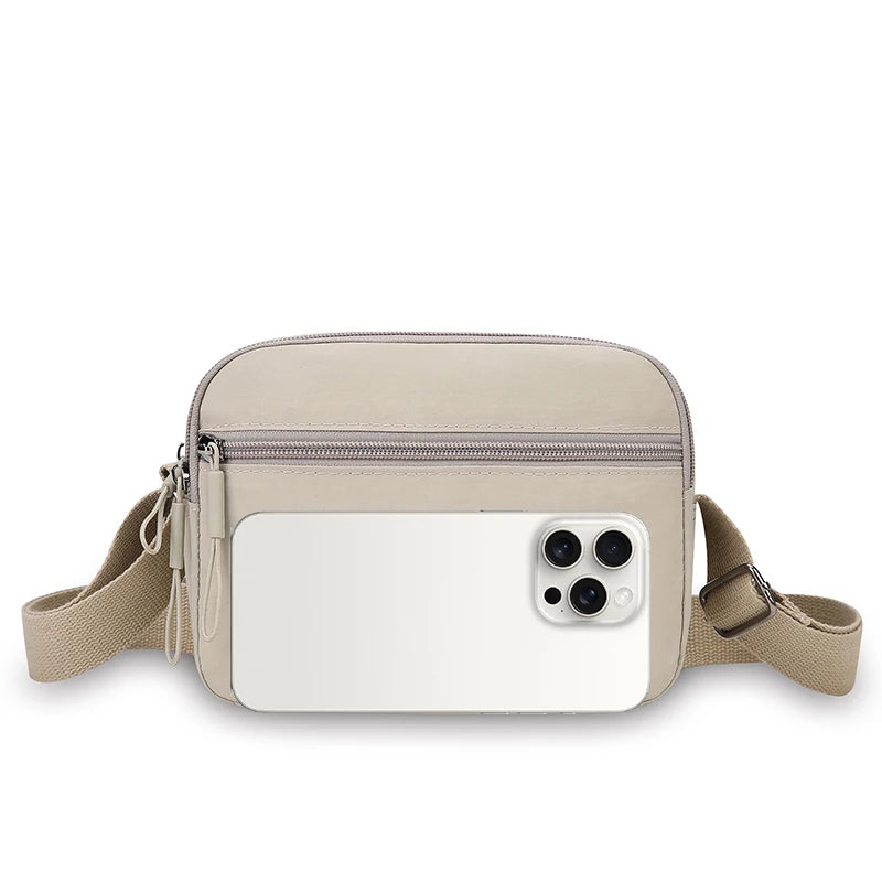 A beige nylon crossbody bag with a wide adjustable strap and a rectangular white phone holder.