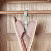 A light pink and beige multi-functional hanging hook is suspended from a wooden bar inside a cabinet.