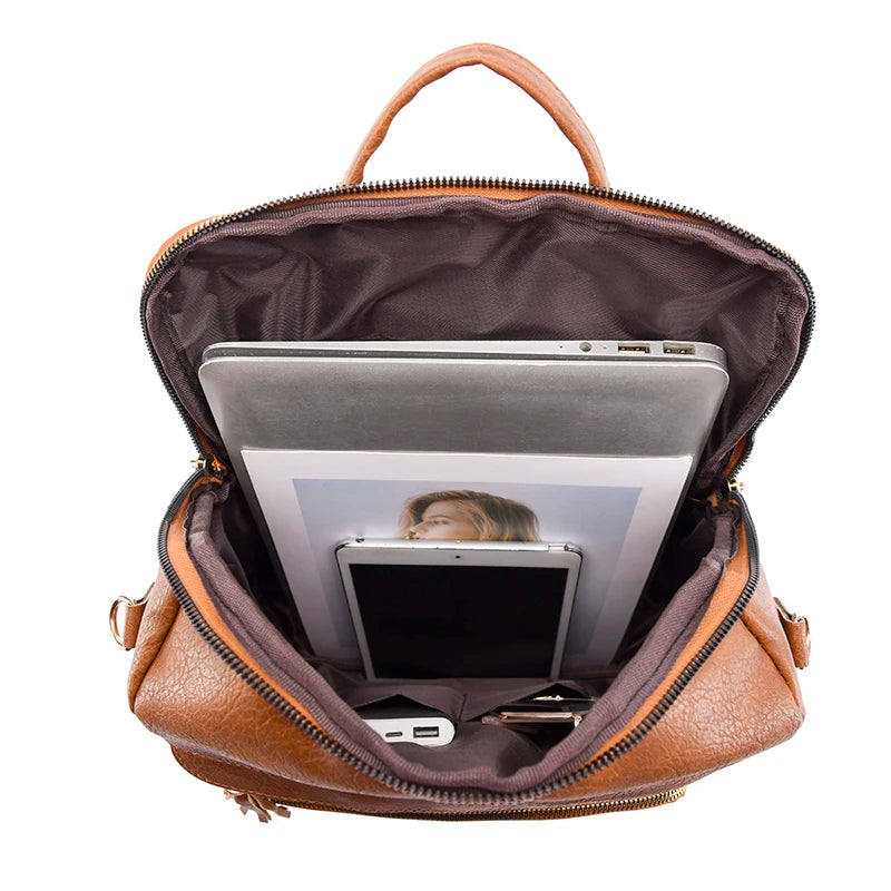 A brown leather backpack with a zipper opening showing a silver laptop and a black tablet inside.