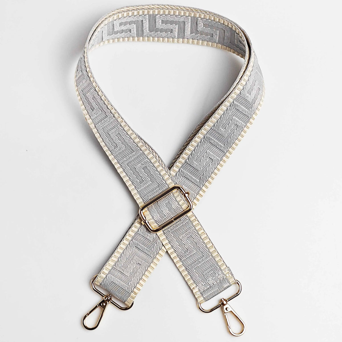 A beige and gray patterned adjustable crossbody bag strap with a gold-toned buckle.