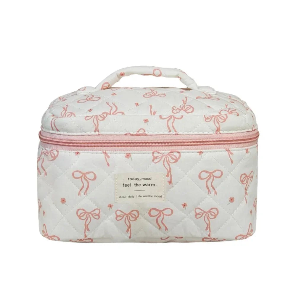 A white quilted cosmetic bag with pink trim and a floral pattern, featuring a handle.