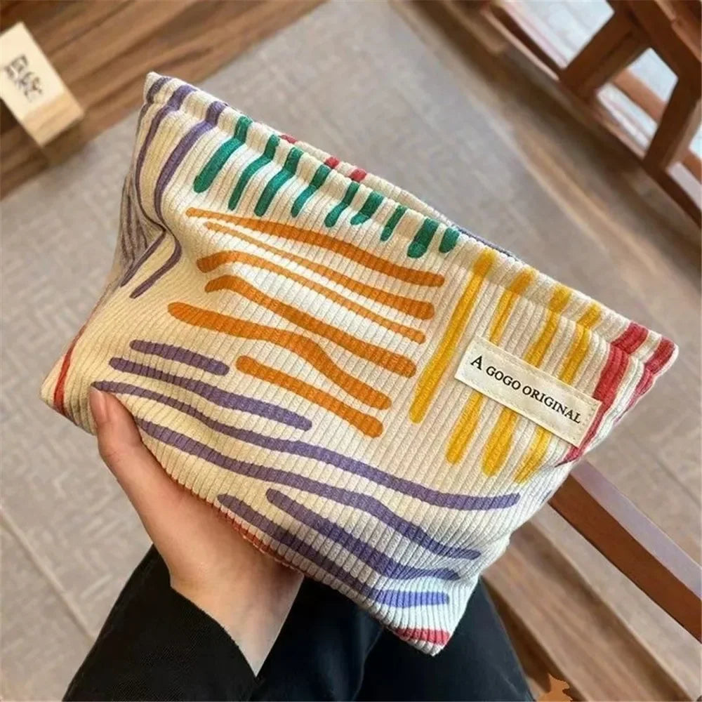 Una bolsa de almacenamiento con cremallera de lienzo y rayas multicolores sostenida en la mano de una persona.