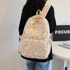 A cream-colored nylon backpack with pink bow prints is carried by a person against a white background.