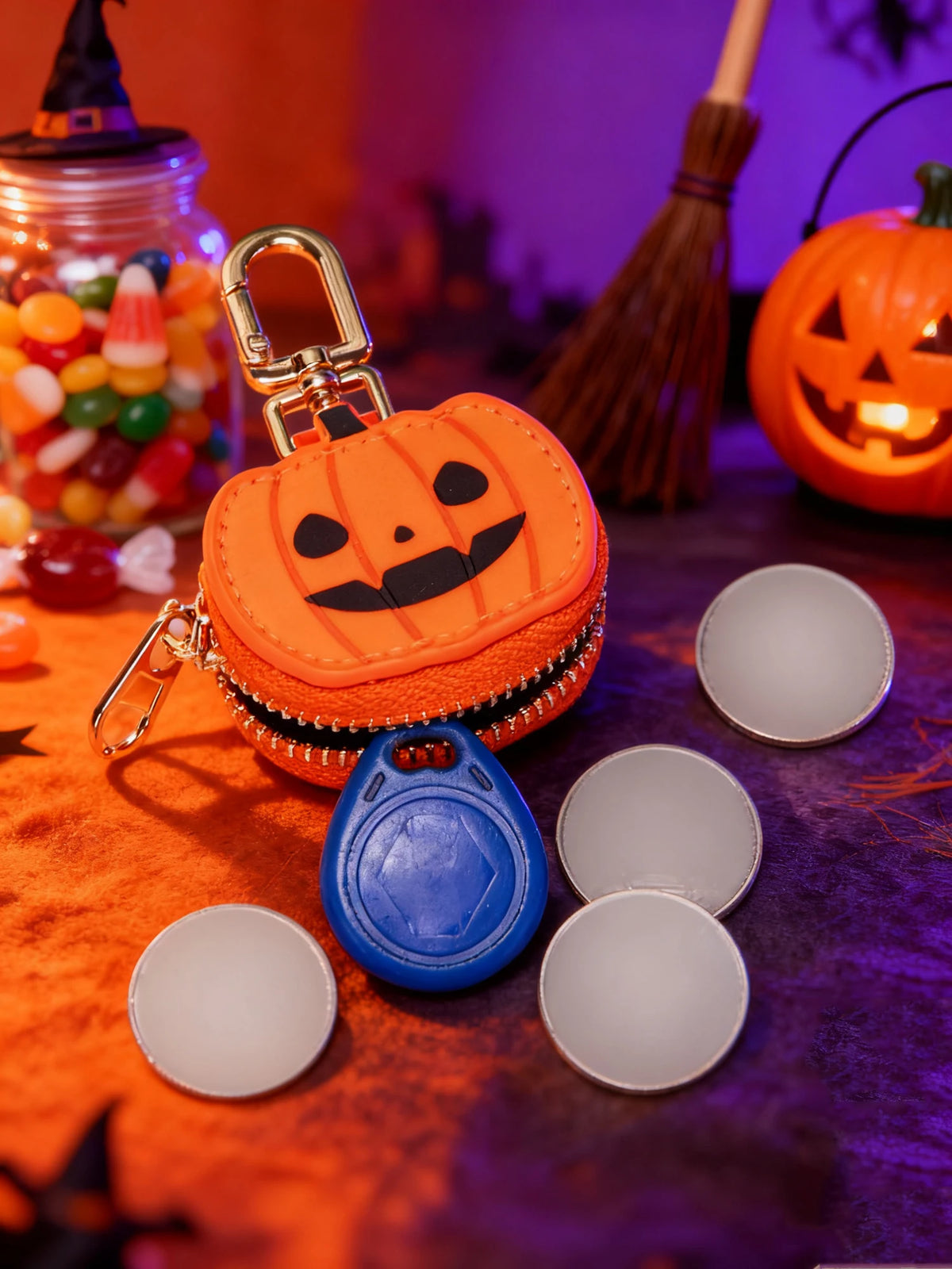 An orange pumpkin shaped mini PU leather keychain accessory rests on a purple fabric surface with other small items.