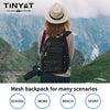 A woman wearing a black mesh backpack is standing outdoors in a mountainous landscape.