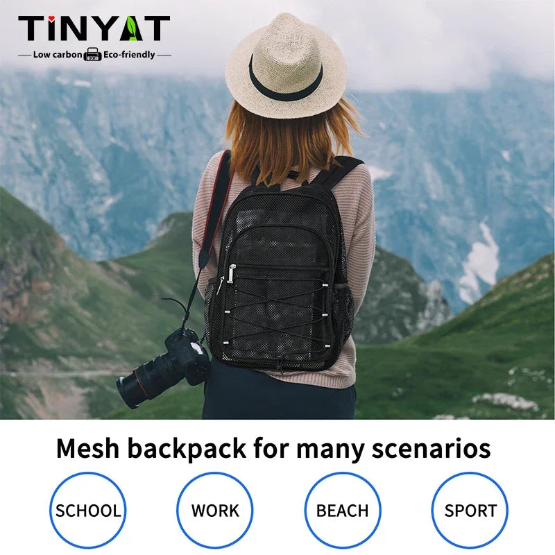 A woman wearing a black mesh backpack is standing outdoors in a mountainous landscape.