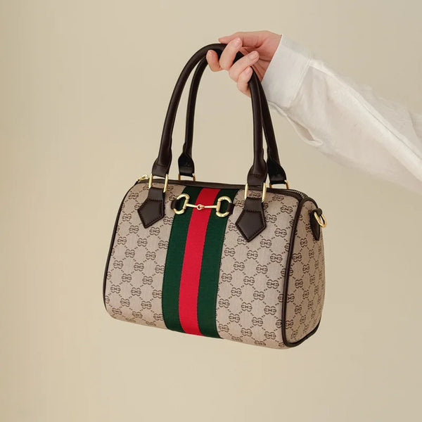 A brown leather tote bag featuring a black and white monogram pattern with green and red stripes, held by a hand.