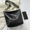 A black leather shoulder bag with a patterned embroidered strap resting on a white surface next to a smartphone.