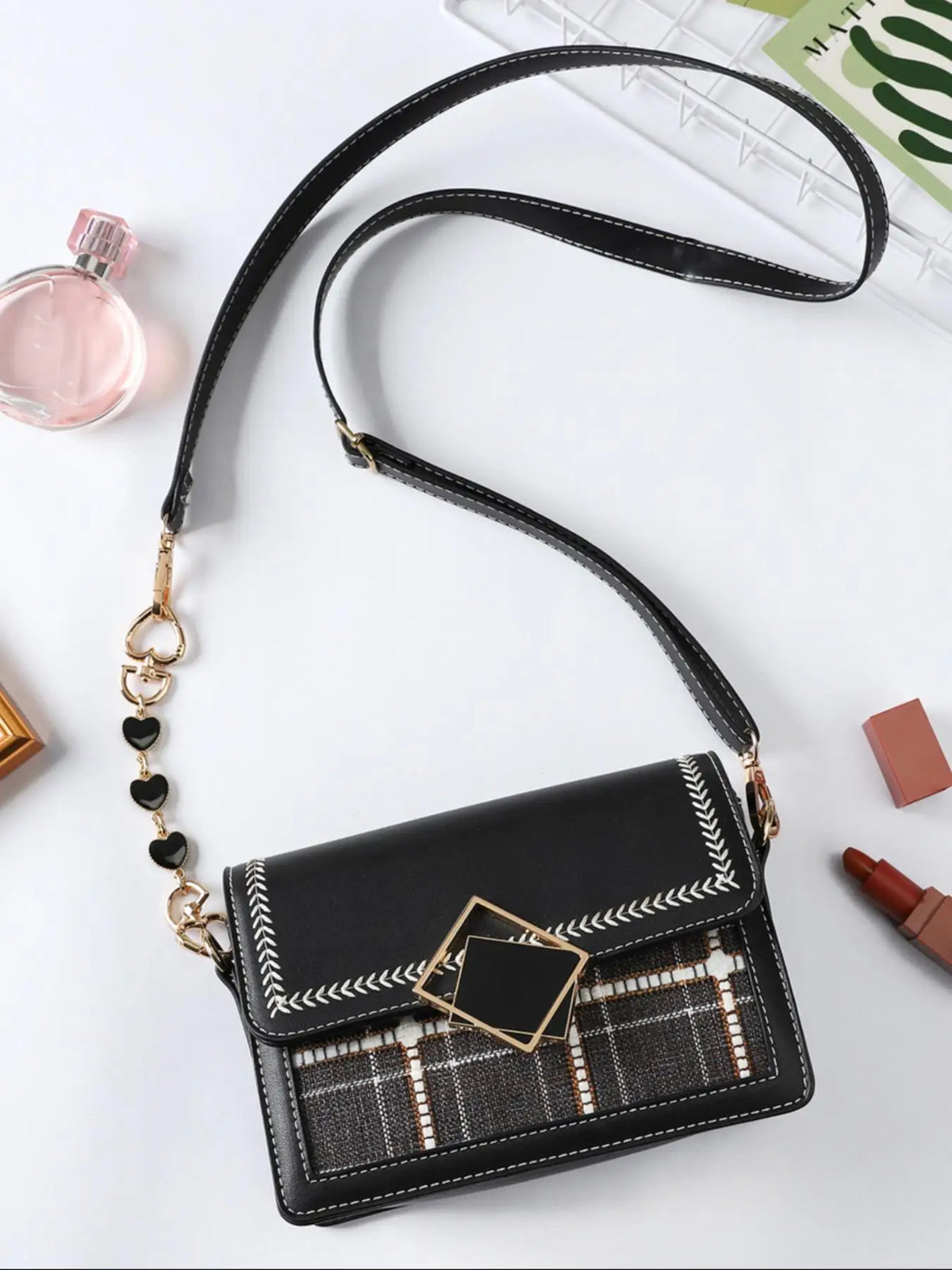 Un sac à main en cuir noir avec un rallonge de chaîne dorée et un fermoir en forme de diamant, exposé sur une surface blanche