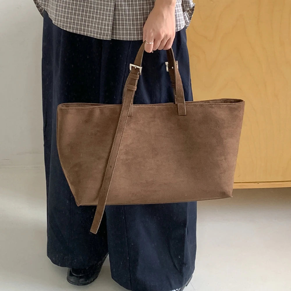 Un sac cabas en cuir PU marron est tenu par une personne portant un pantalon foncé.