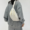 A woman wearing a gray sweatshirt carries a cream-colored corduroy waist pack on her shoulder.