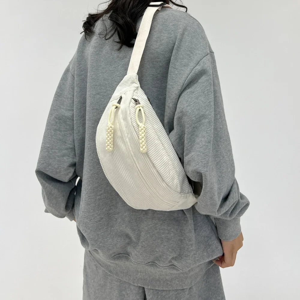 A woman wearing a gray sweatshirt carries a cream-colored corduroy waist pack on her shoulder.
