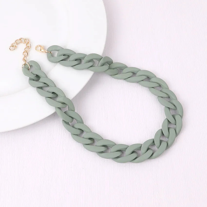 A close-up of a trendy acrylic statement choker necklace in a sage green chain resting on a white surface.